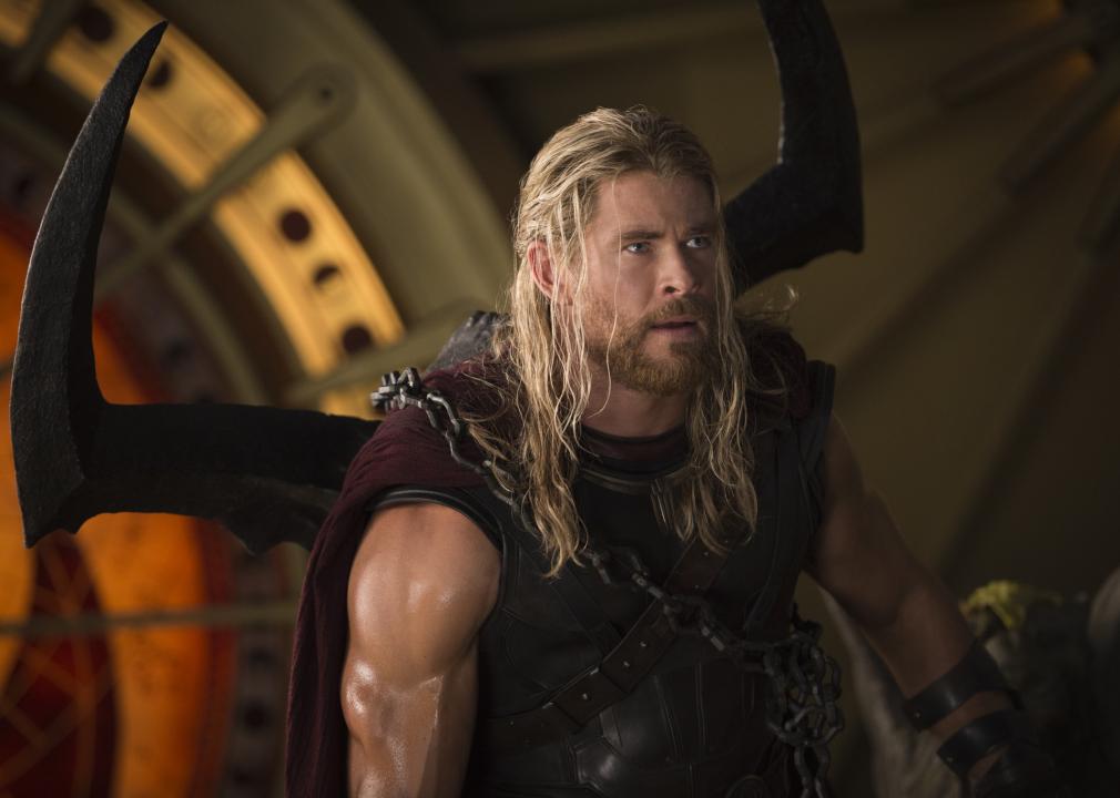 A muscular man with long blonde hair wears armor and chains.