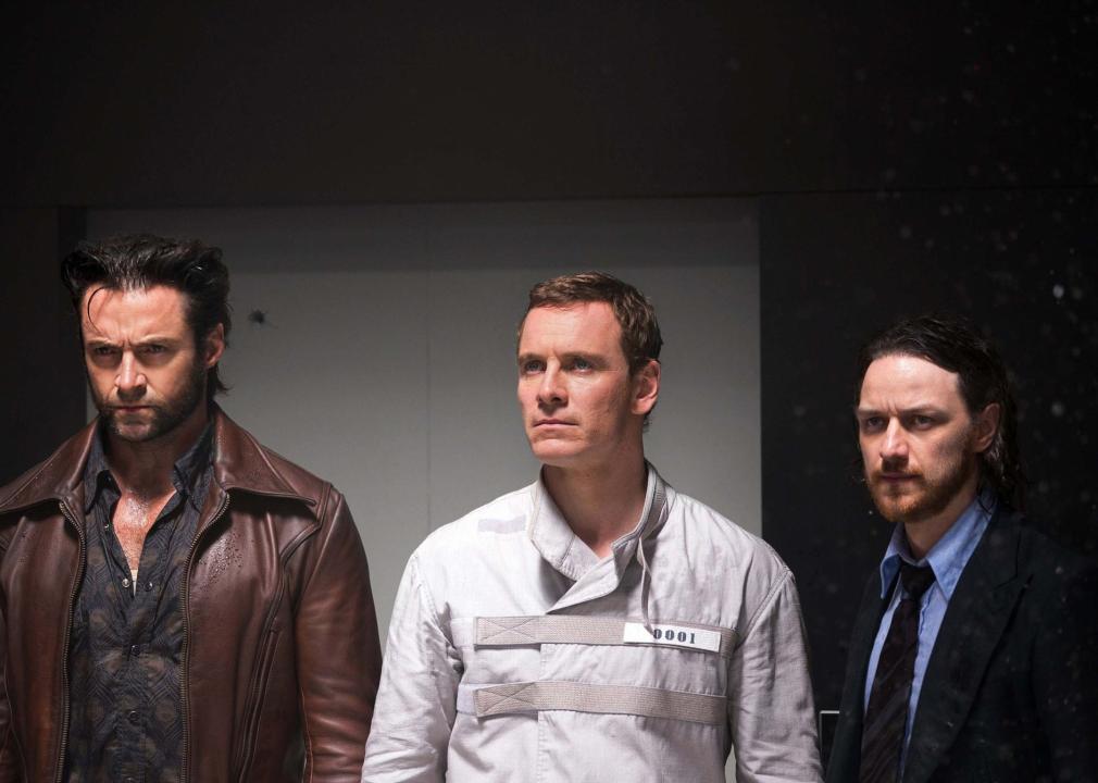 3 men stand looking serious, one in a leather jacket, one in a straightjacket and another in a suit.