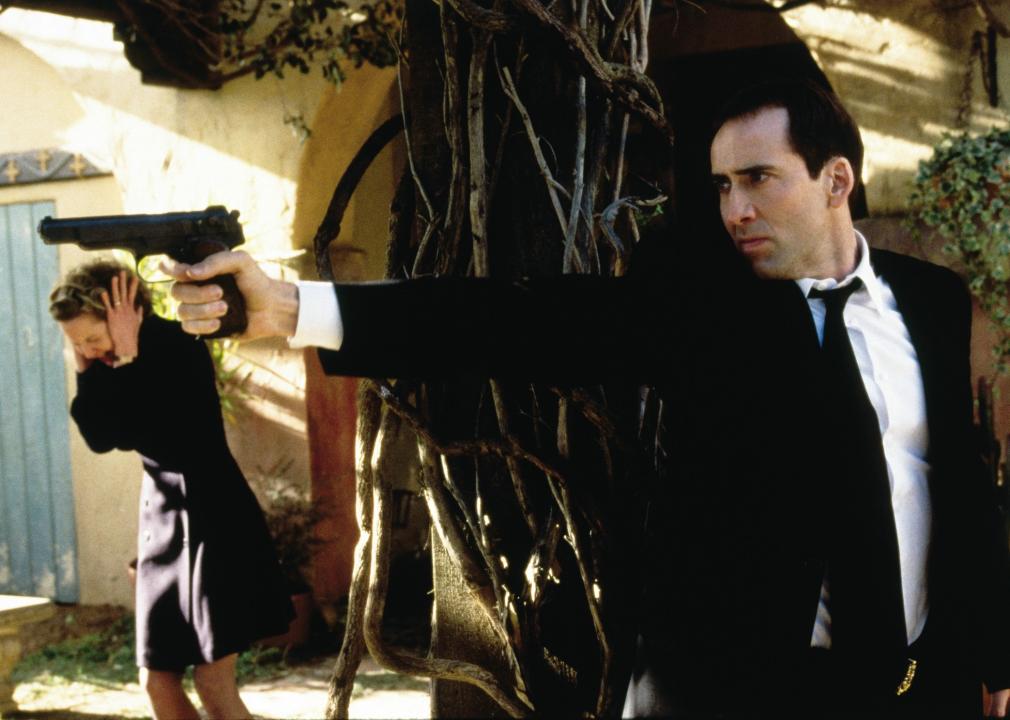 A man pointing a gun with a woman holding her ears in the background.