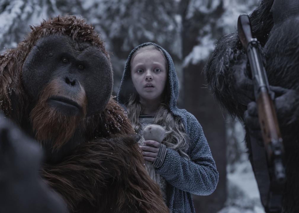 A scared little girl stands in between two apes with guns.
