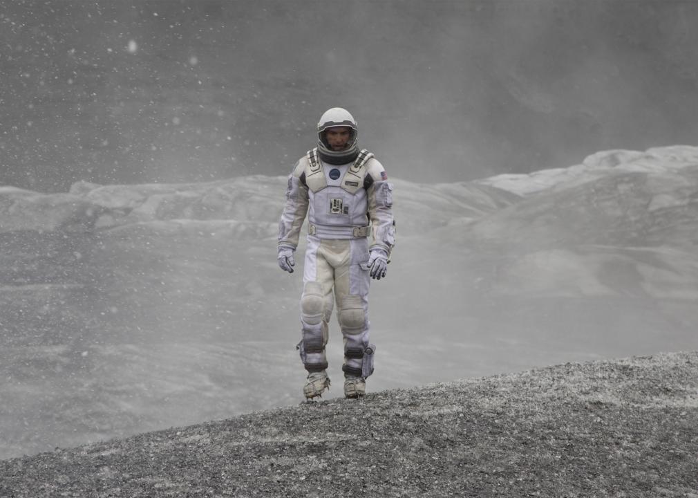 A man in a space suit walks through weather on another planet.