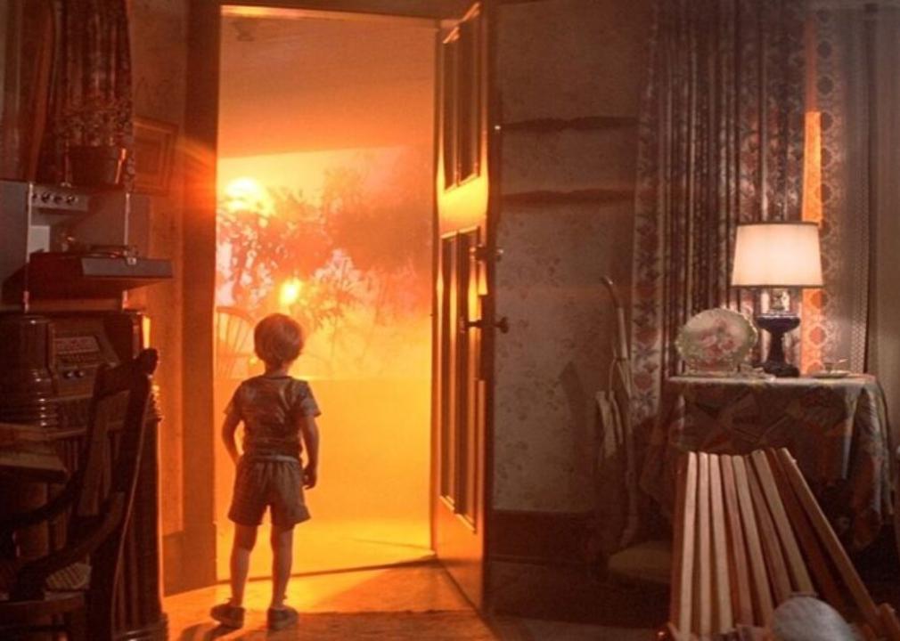 Little boy looking out the open front door of his home with a bright orange light illuminating everything.