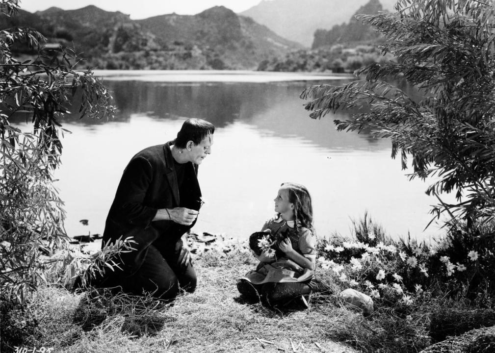 Frankenstein sitting next to a little girl by a pond.