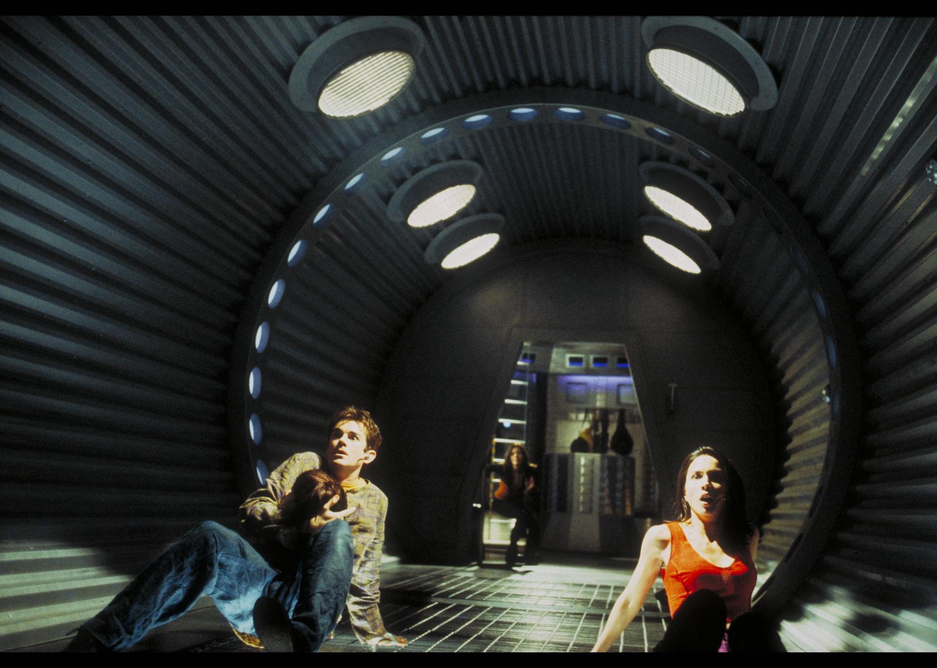 A young man and woman looking scared in a wide metal tubular tunnel.