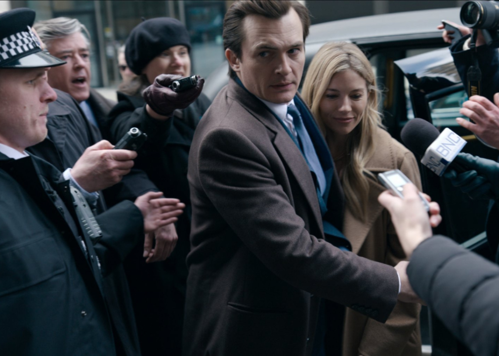 Man and woman stepping out of a car and being bombarded by cameras andd microphones.