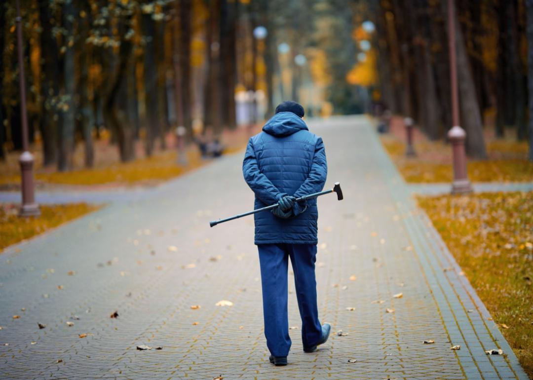 An elderly man walking on a path through a city.