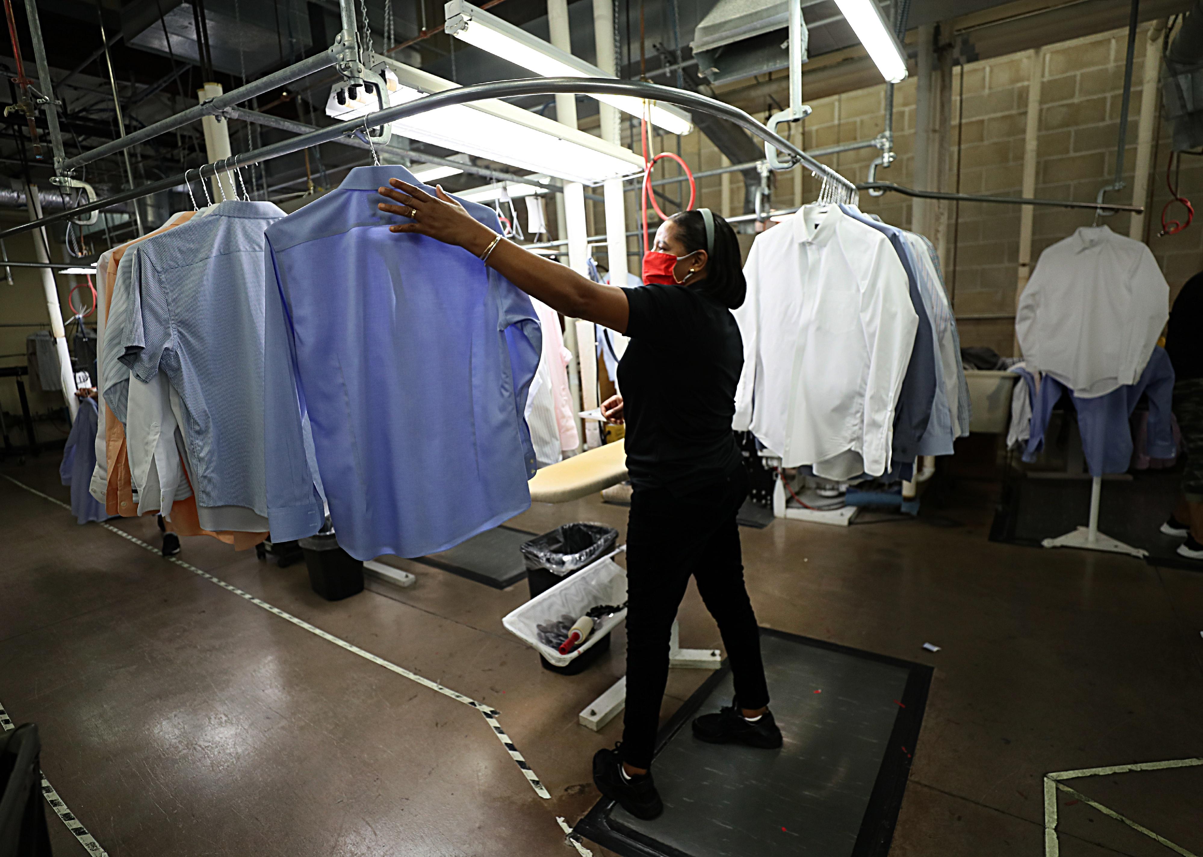 A masked woman working at a dry cleaner.