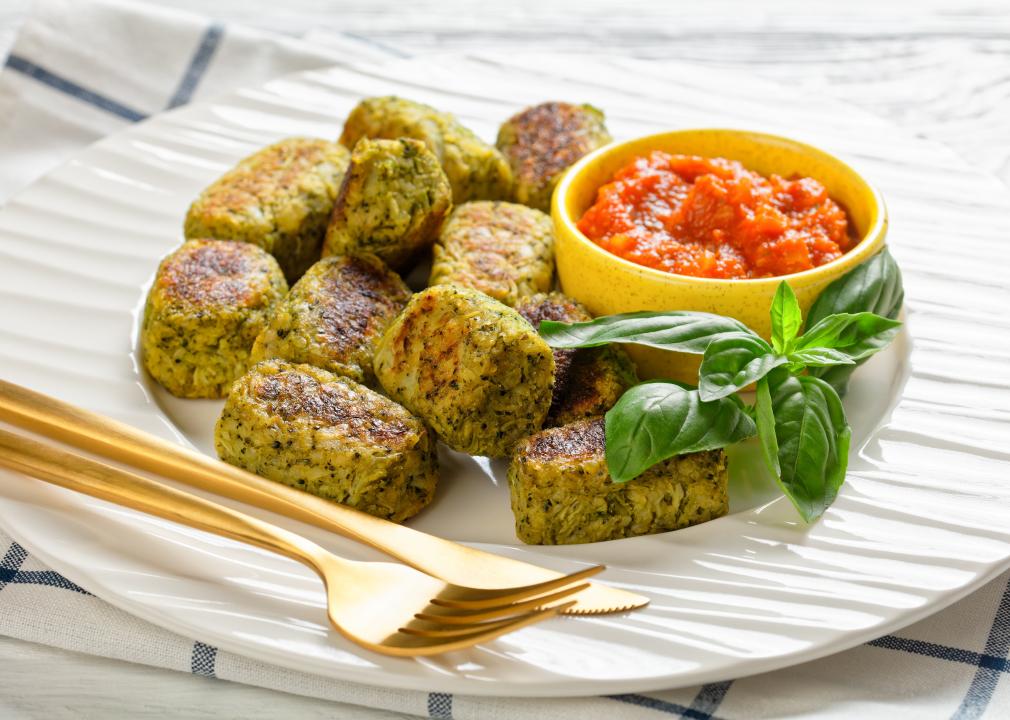 A white plate full of veggie tots with salsa on the side and gold silverware.