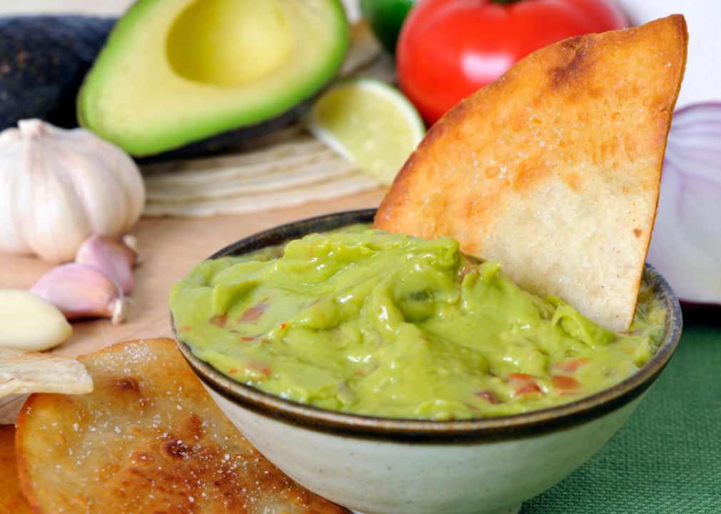 Homemade tortilla chips and a bowl of guacamole with garlic and avocado in the background.