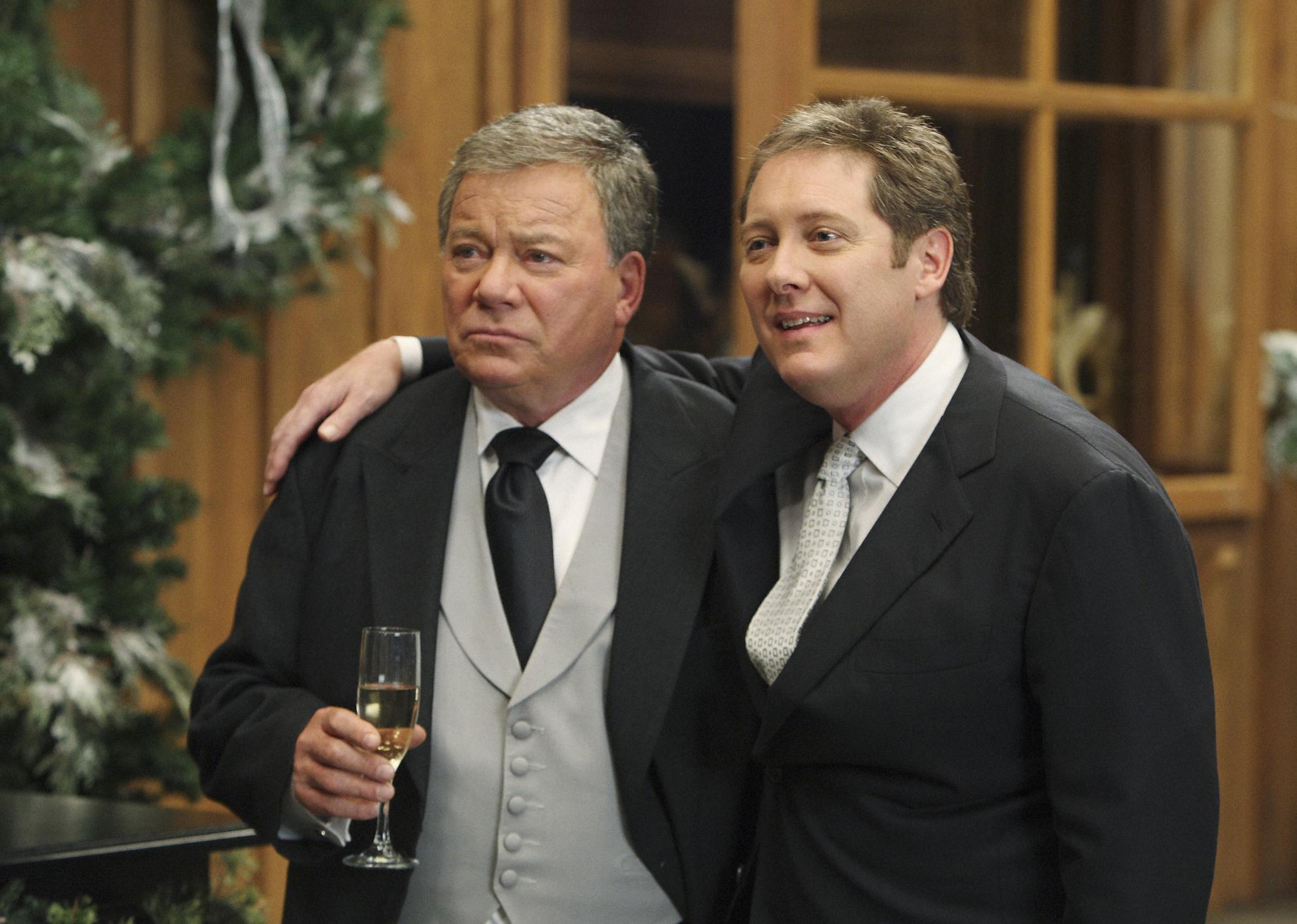 William Shatner and James Spader arm in arm wearing suits and holding champagne.