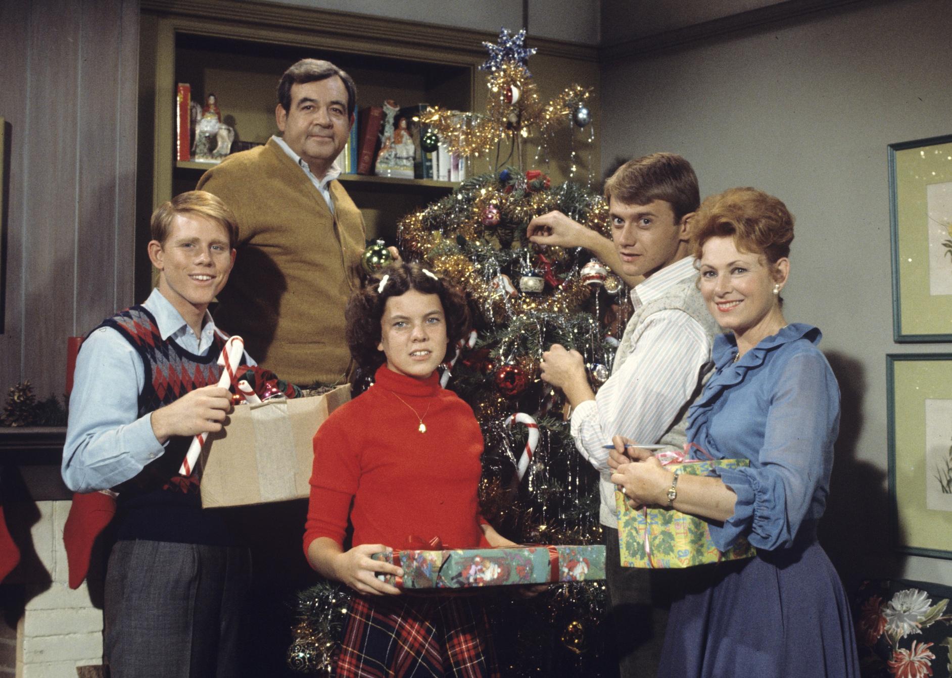 A family decorating and posing in front of a Christmas tree.