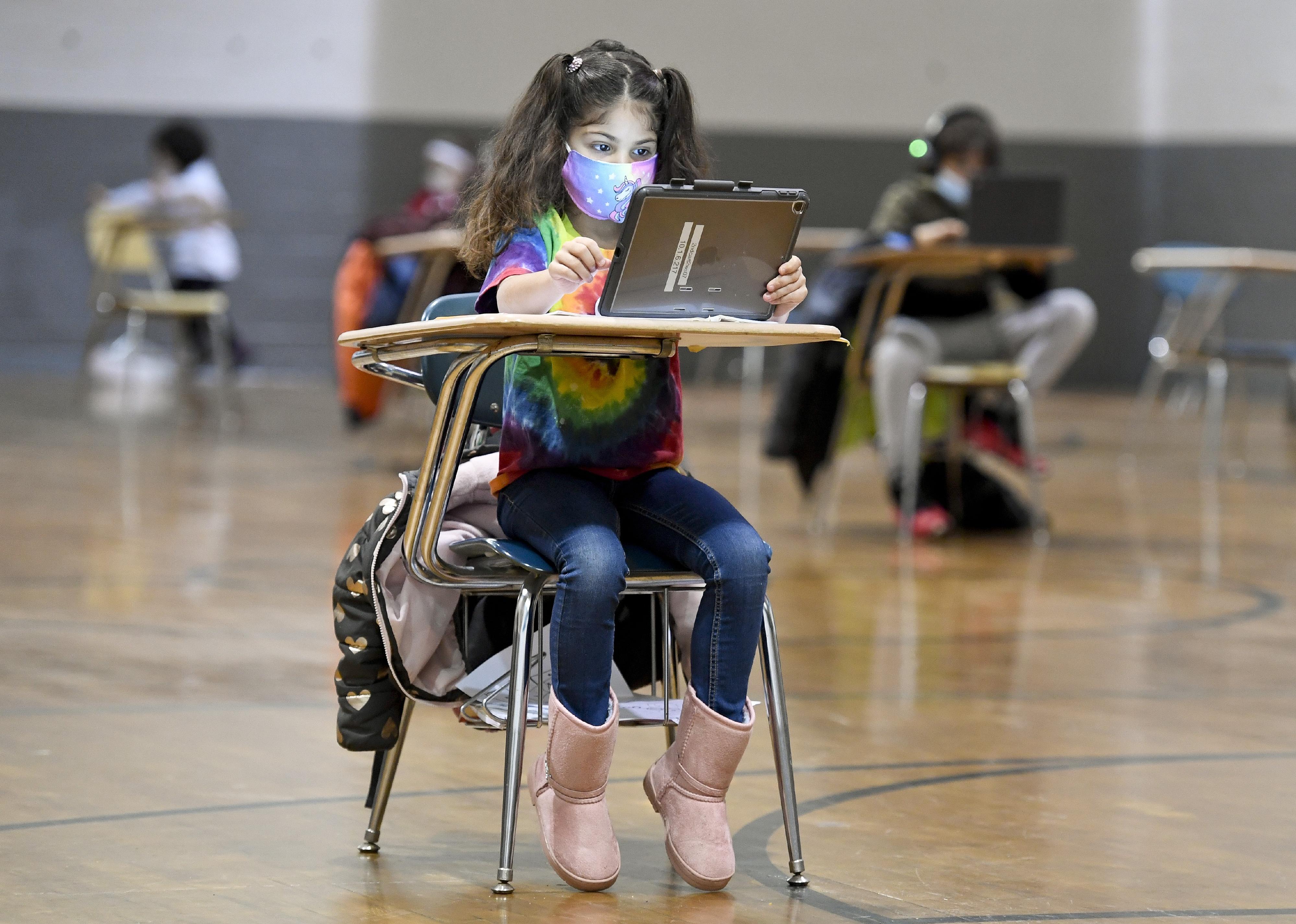 A young student sitting at a desk distanced from her classmates in the gym.