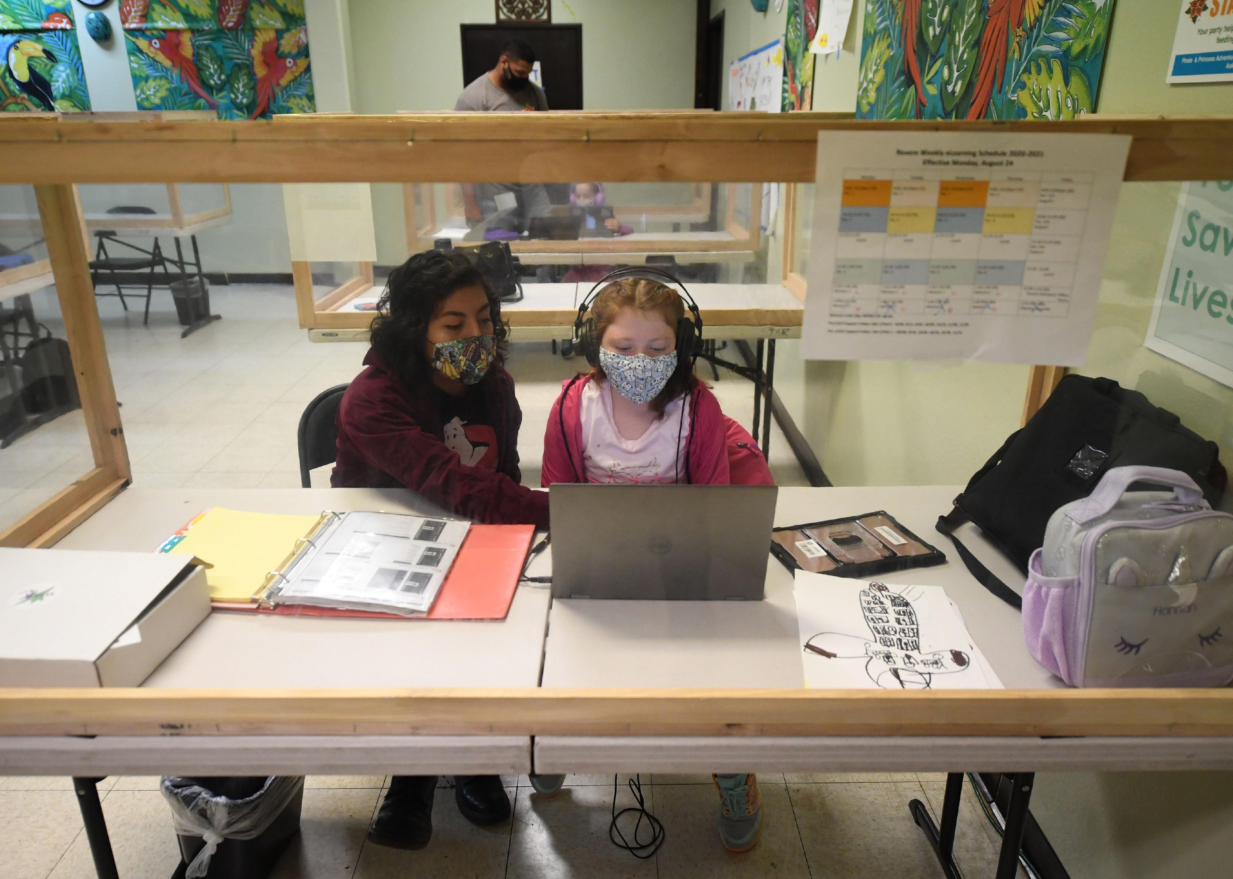 A woman tutoring a young girl in a classroom.