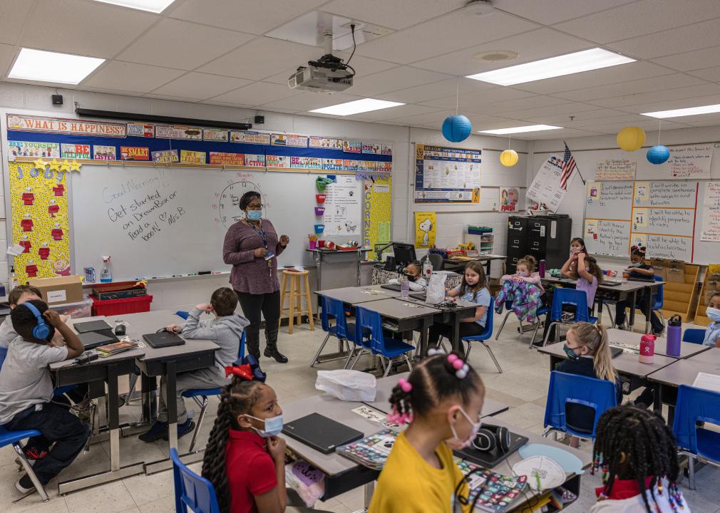 A second grade teacher starts class and students look up at her from desks.