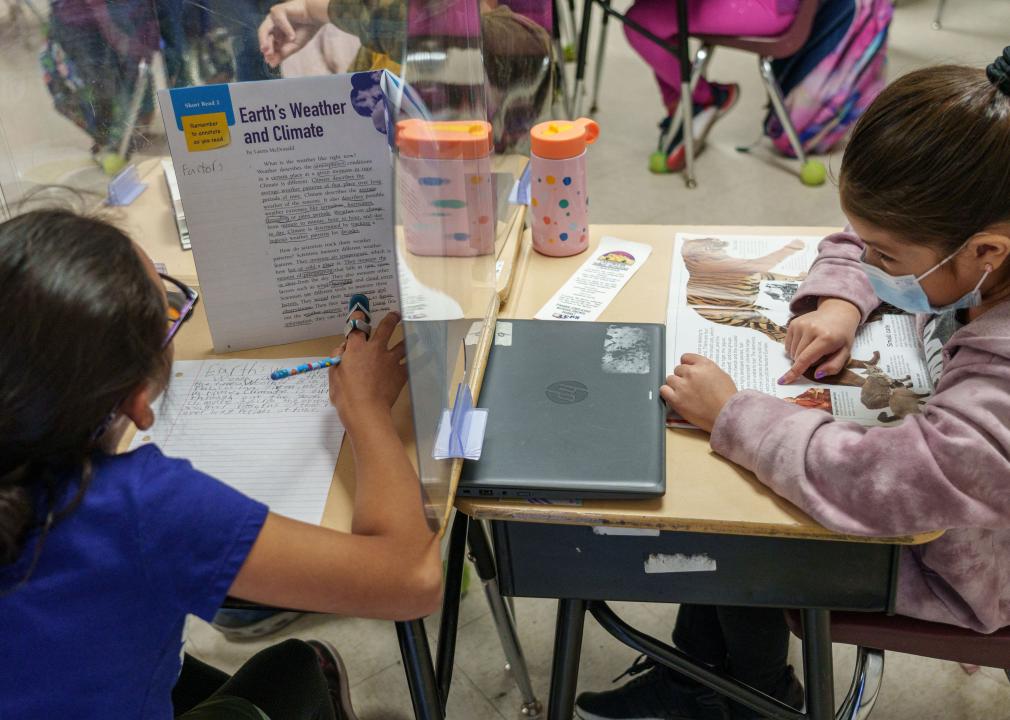 Two third grade girls work on assignments in class, one with an animal book and the other with a weather book.