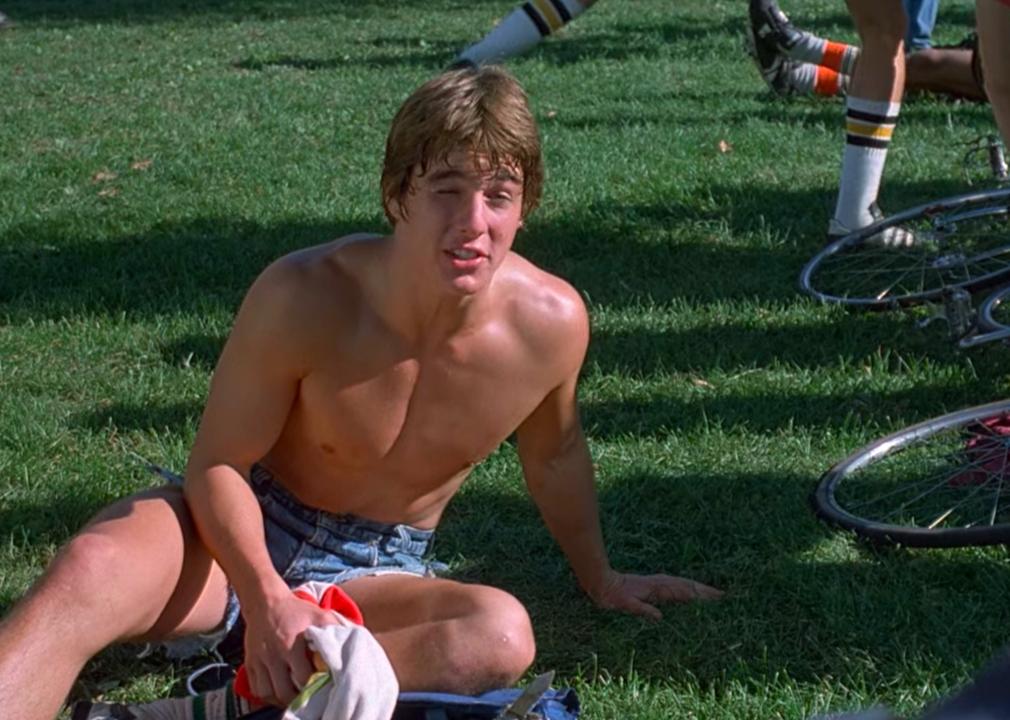 Tom Cruise sits on the grass shirtless.