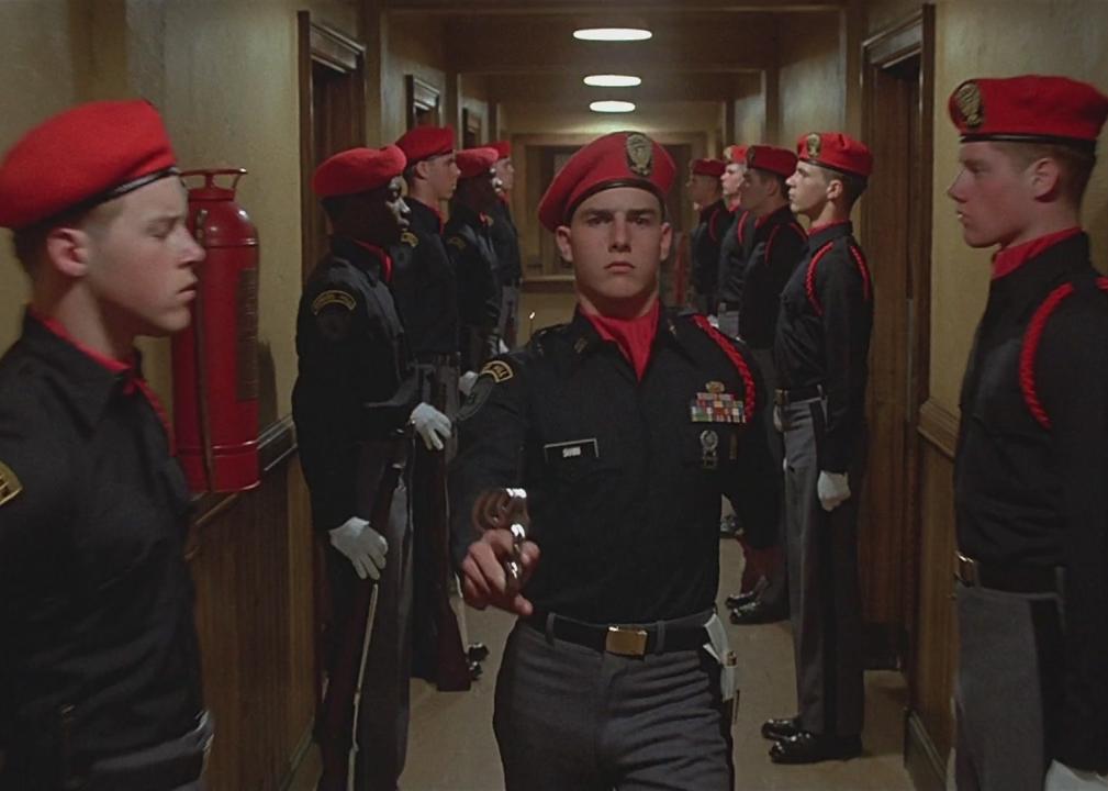 Tom Cruise, wearing military uniform, walks down a hallway lined with military.