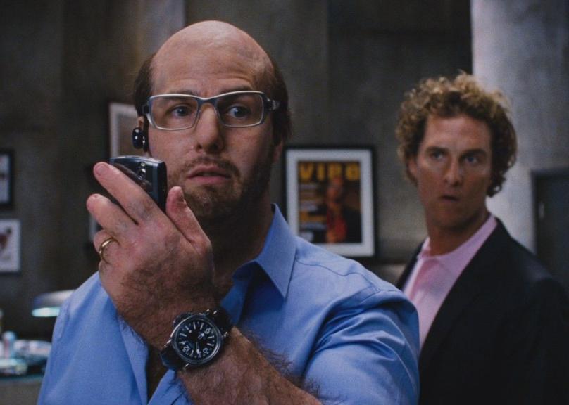 A balding Tom Cruise talks on the phone with Matthew McConaughey in the background.