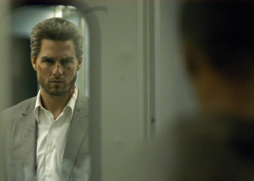 Tom Cruise, with salt and pepper hair and a grey suit, looks at someone through a subway car door.