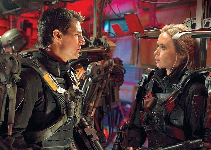 Tom Cruise and Emily Blunt, dressed in dark armor, look seriously at each other.