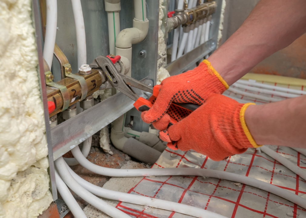 A pipefitter wearing orange gloves tightening pipes.