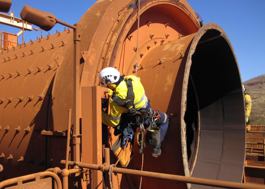 A boilermaker wearing a safety harness, hanging on a rope at a construction mining site.