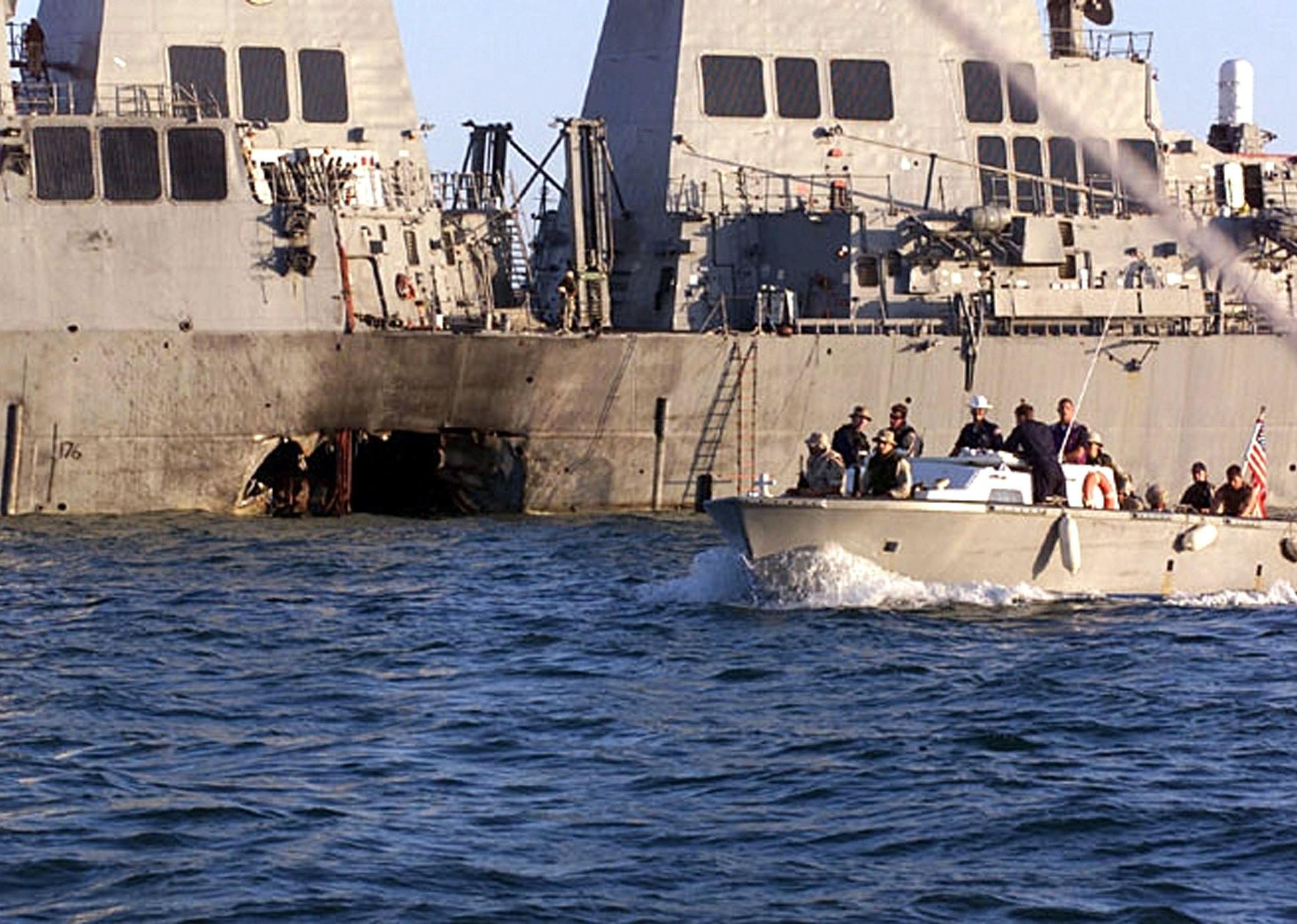 U.S. Navy and Marine Corps security personnel patrol past the damaged U.S. Navy destroyer USS Cole.