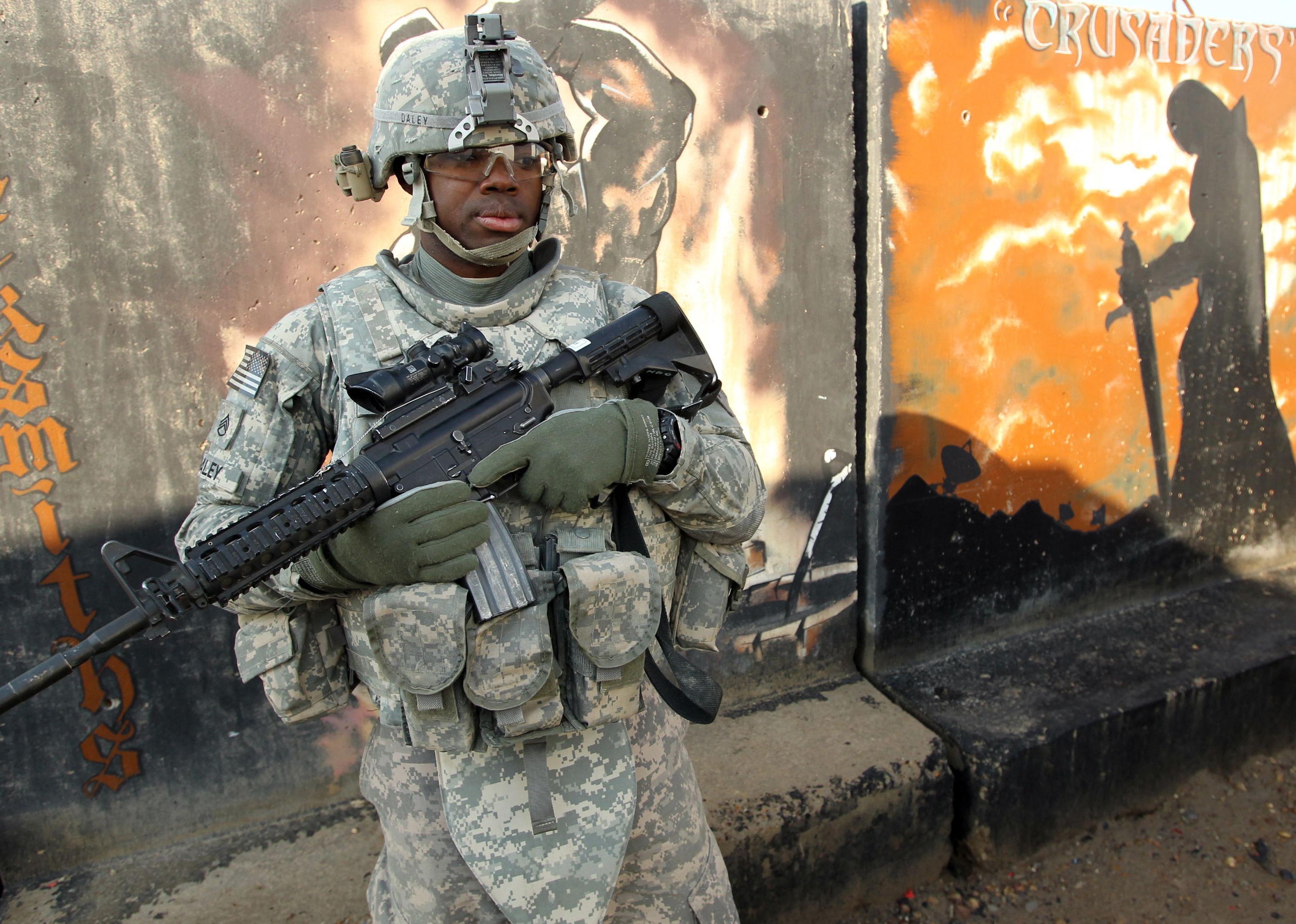 A U.S. soldier stands guard in front of graffiti.