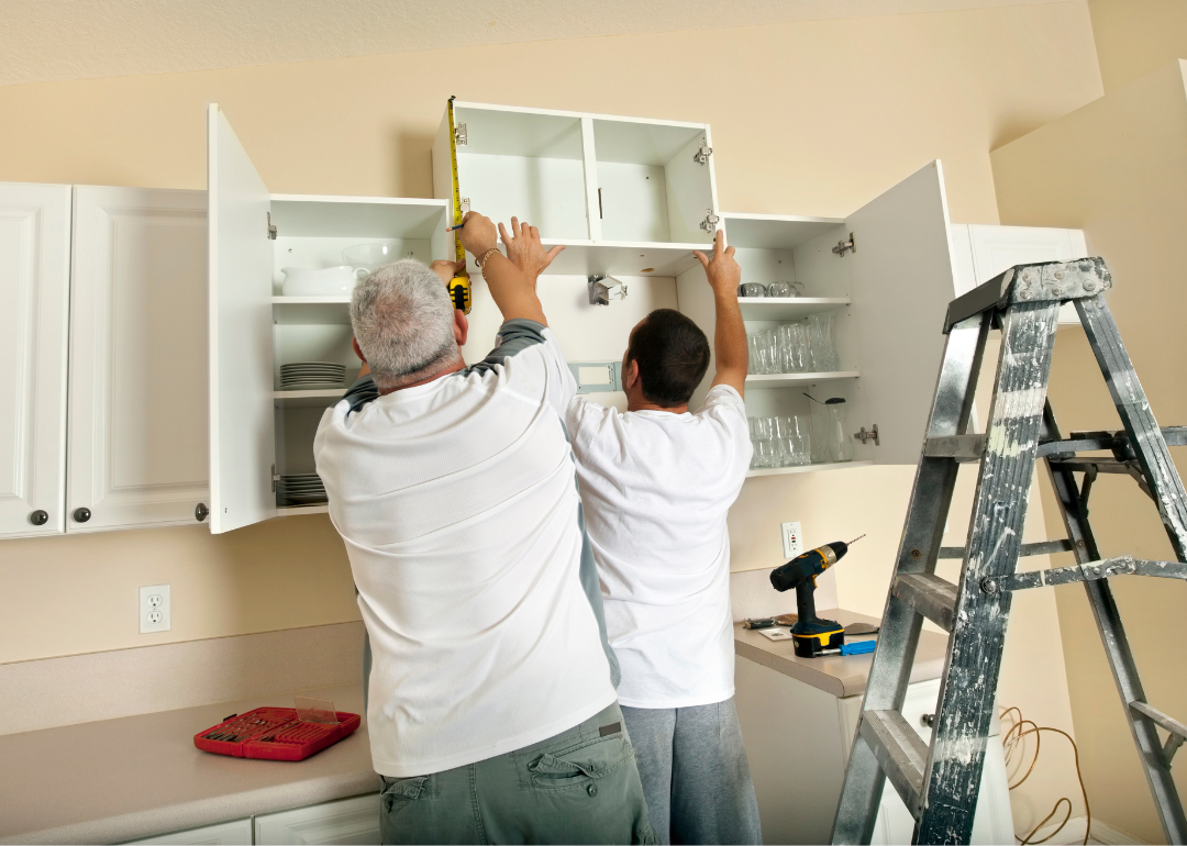 Two people installing white cabinets.