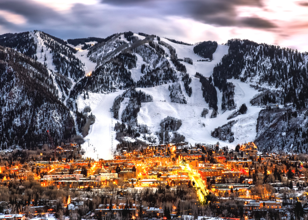 A warmly lit town with snow-covered mountains in the near background.