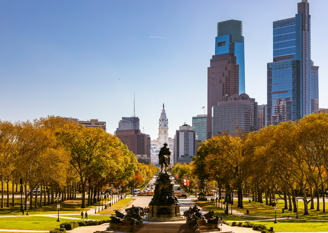 People walking in a tree-lined park in autumn with downtown Philadelphia in the background.