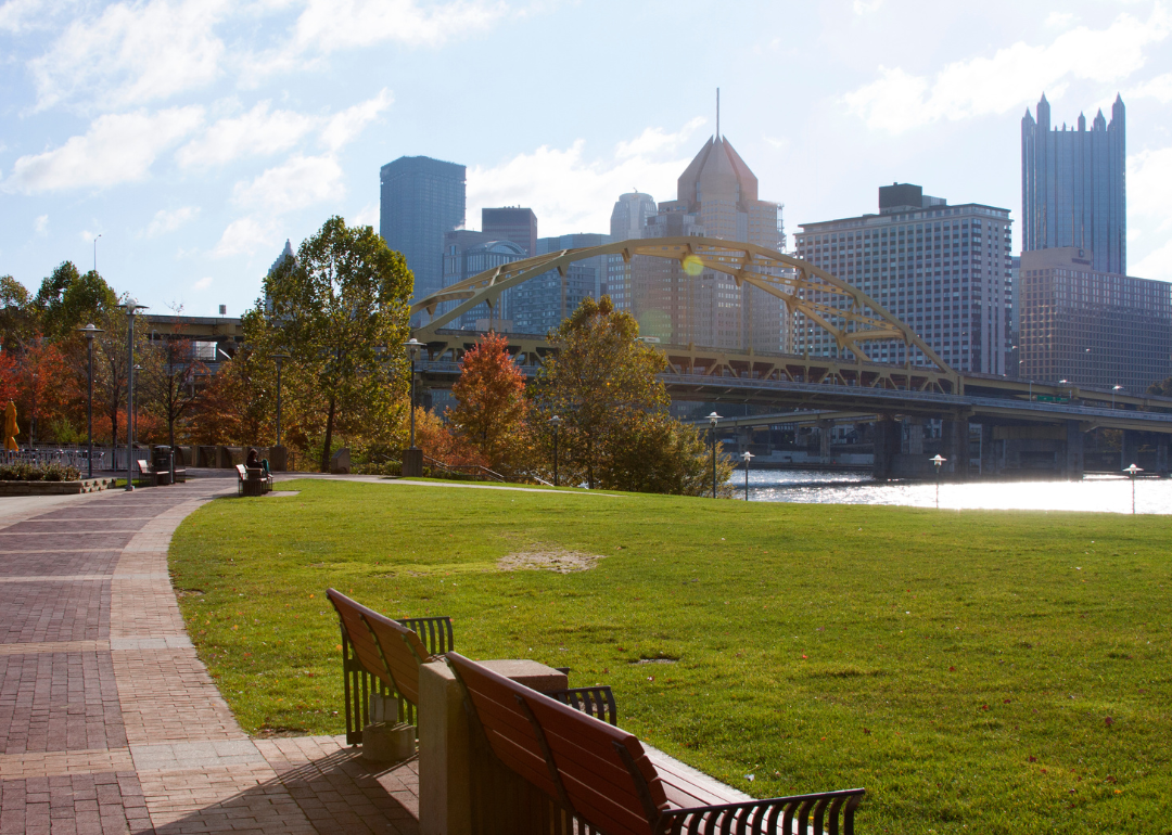 A path in a park with the Pittsburgh skyline across a bridge.