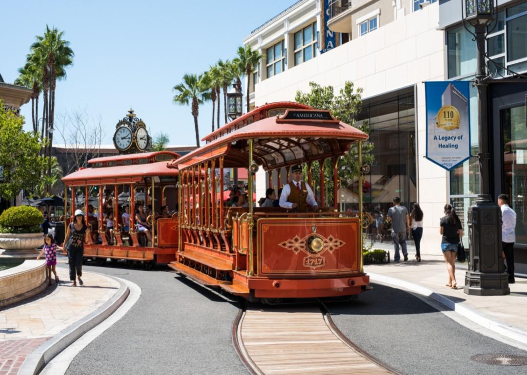 A trolley going through downtown Glendale with pedestrians on the sidewalk.