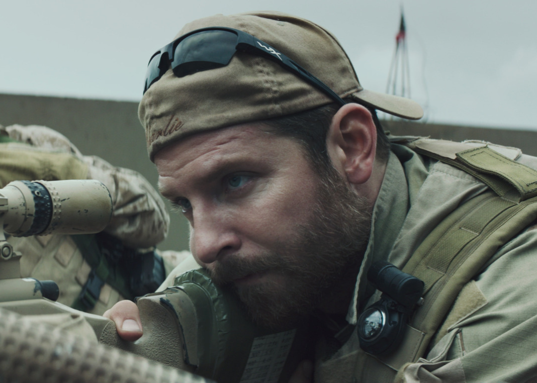 Bradley Cooper looking through the scope of a gun.