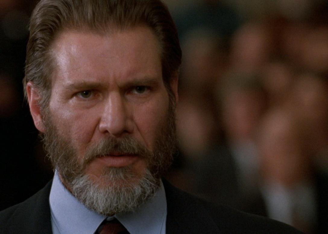Harrison Ford with a beard and slicked back hair in a suit.
