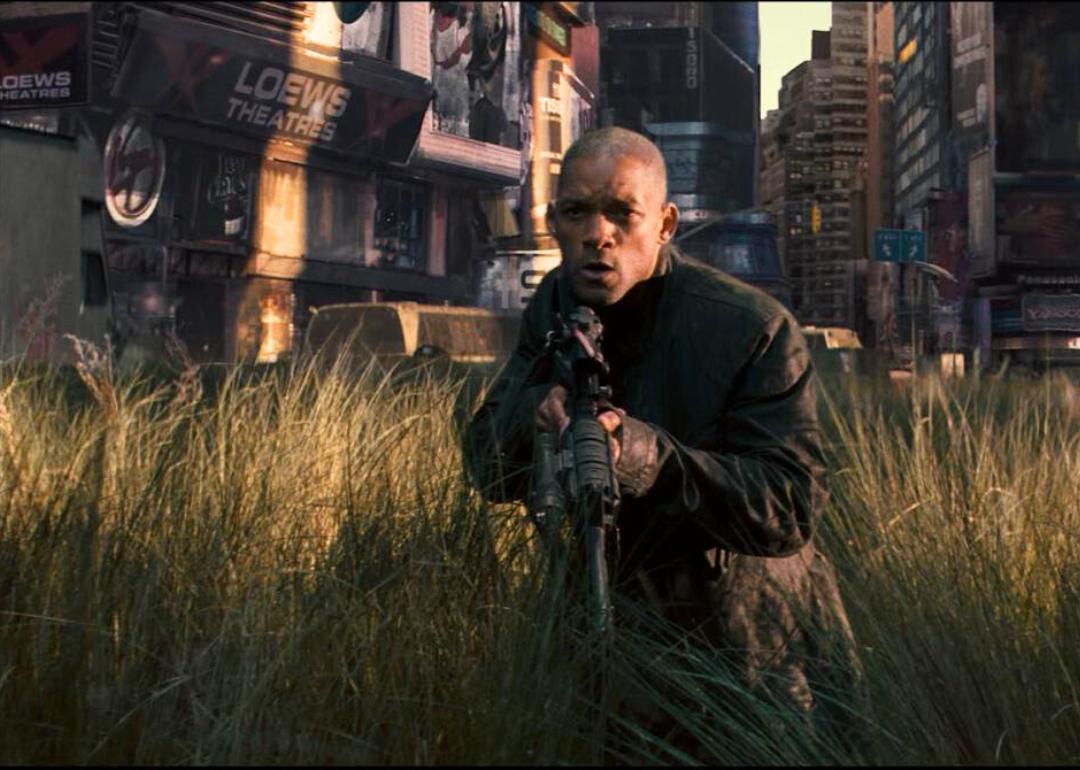Will Smith with a gun walking through an overgrown downtown.