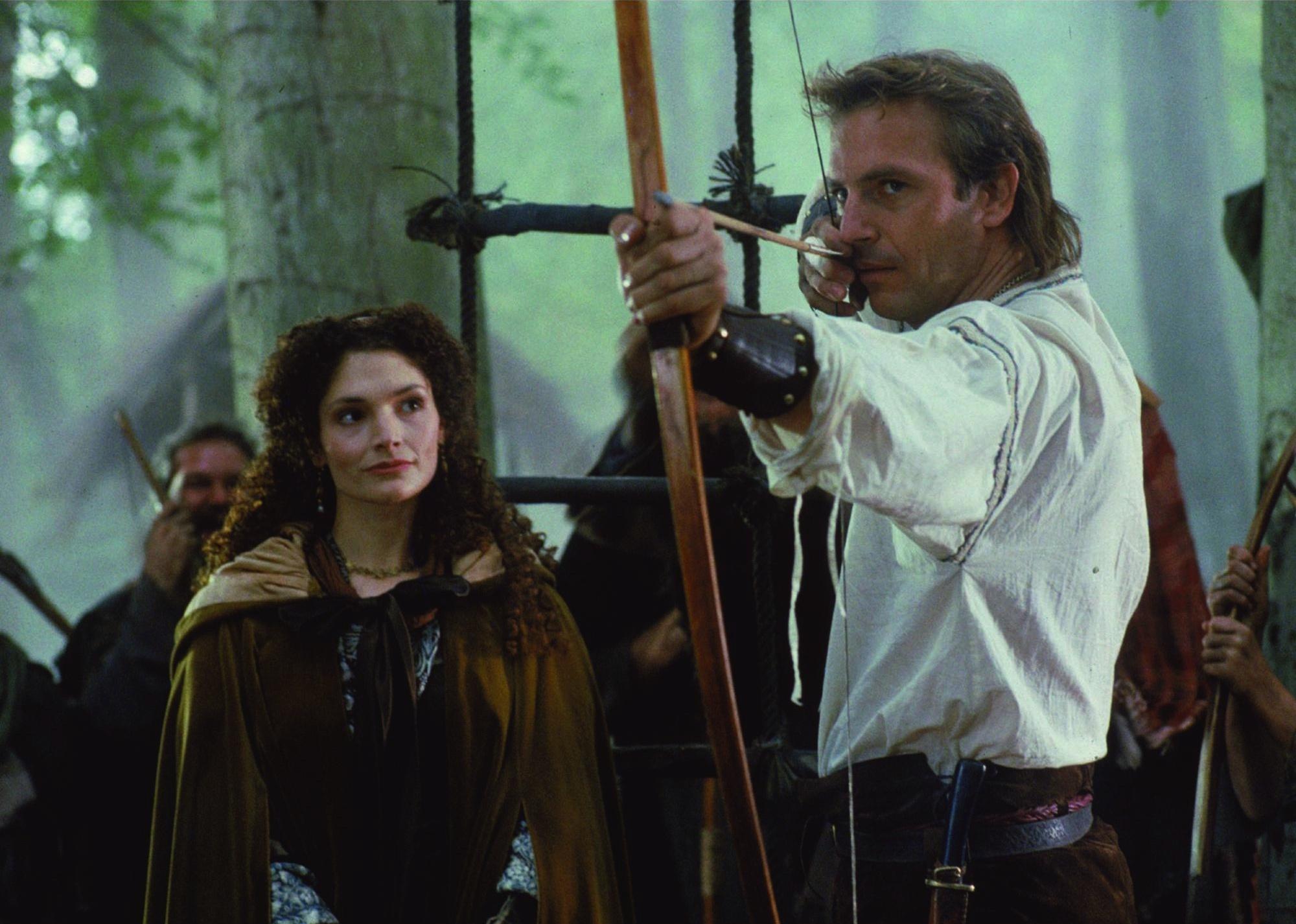 Kevin Costner pointing a bow and arrow.