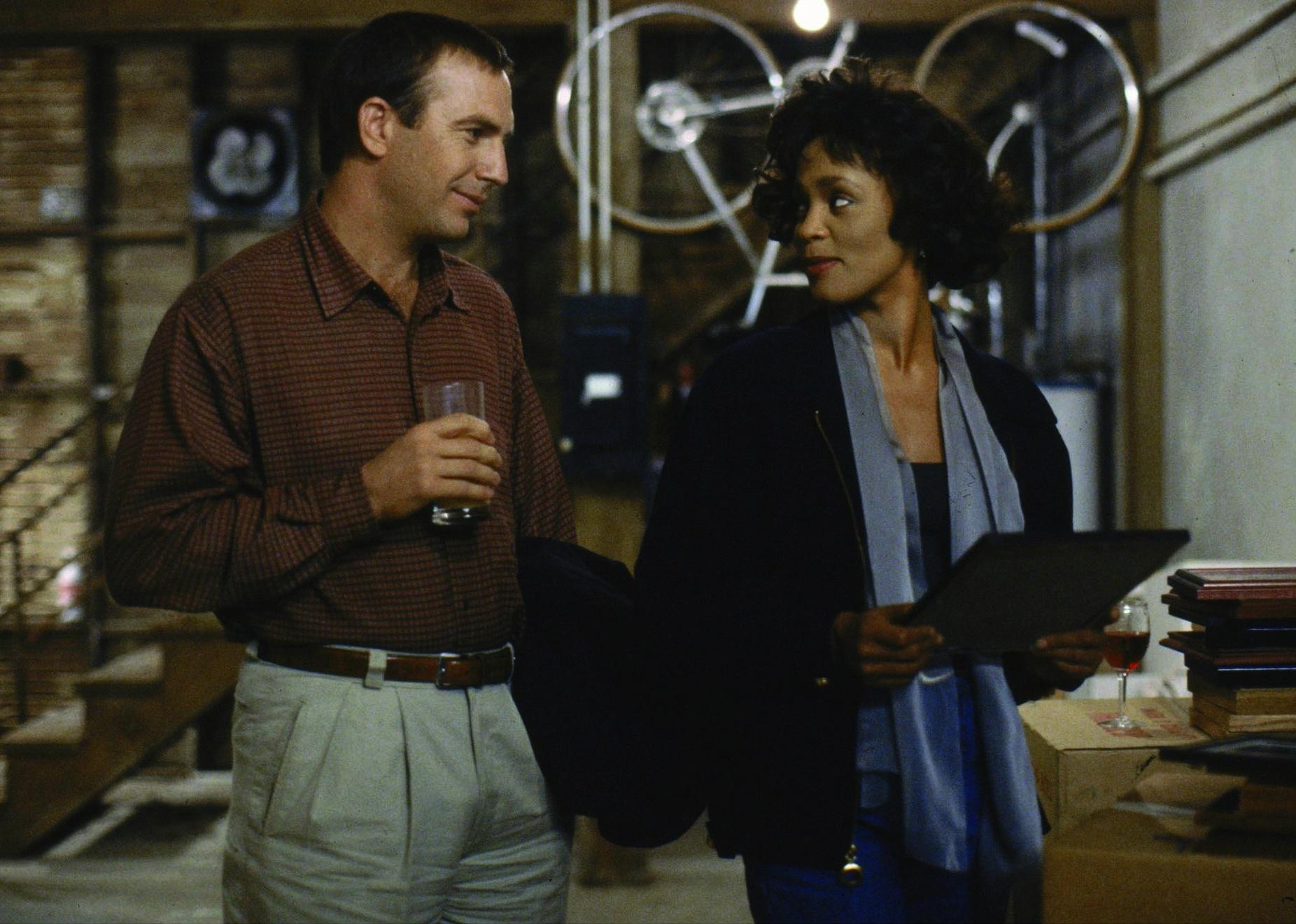Kevin Costner and Whitney Houston smiling at each other.