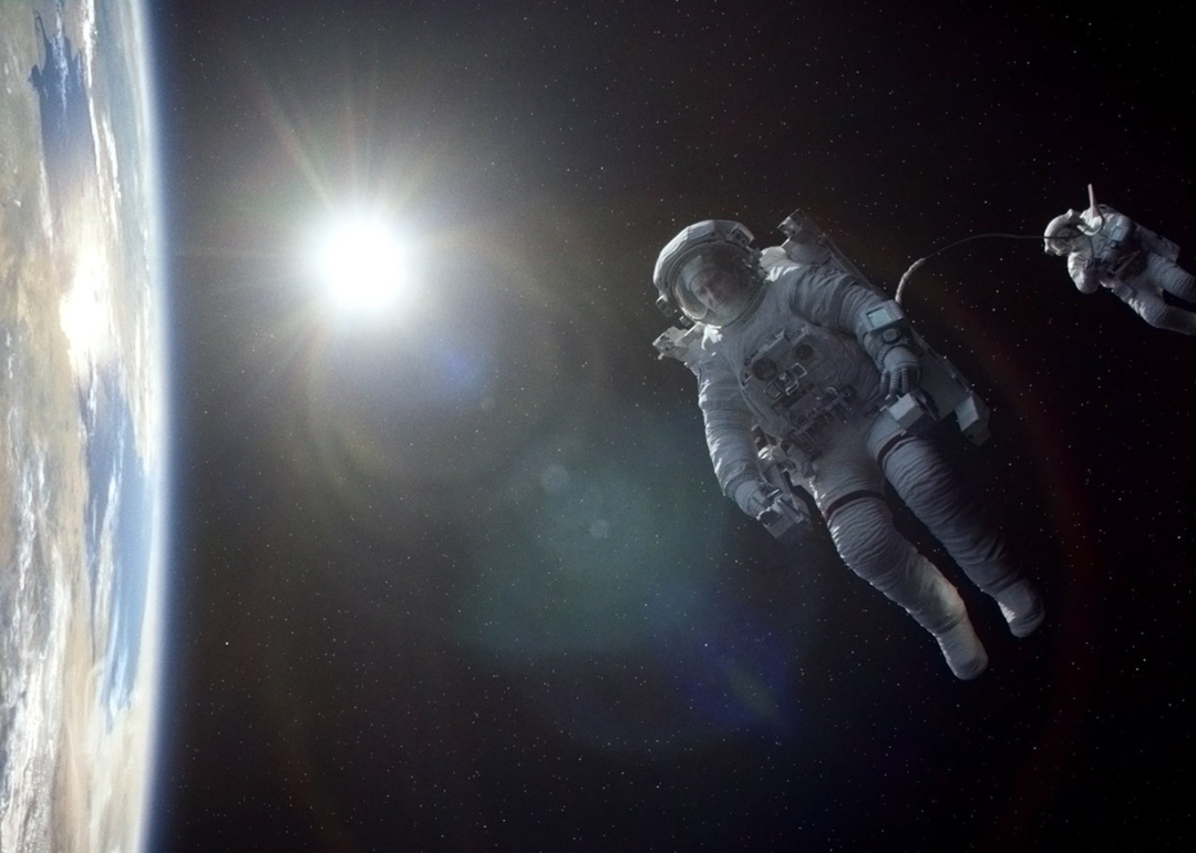 Sandra Bullock and George Clooney floating in space suits with planet Earth below.