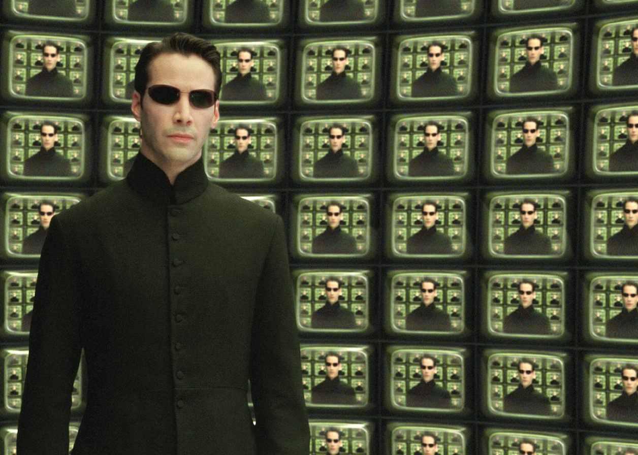Keanu Reeves in all black surrounded by television screens of his mirror image.
