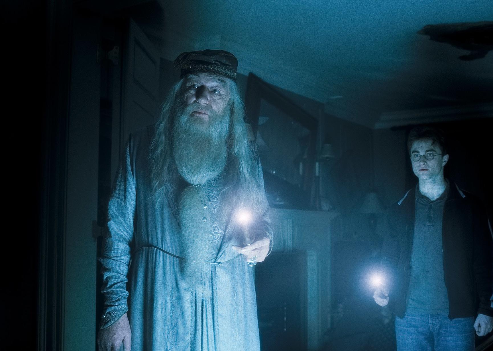 Michael Gambon and Daniel Radcliffe shining flashlights at night in a room.