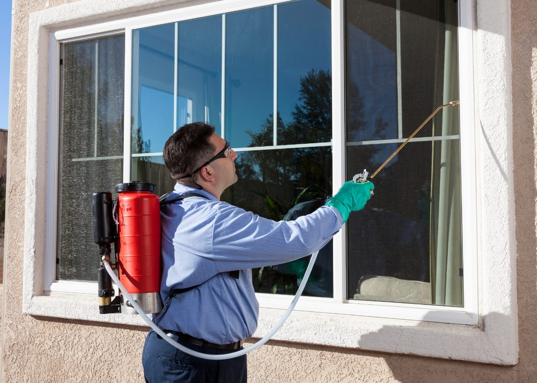 A pest control worker spraying the outside windows of a home.