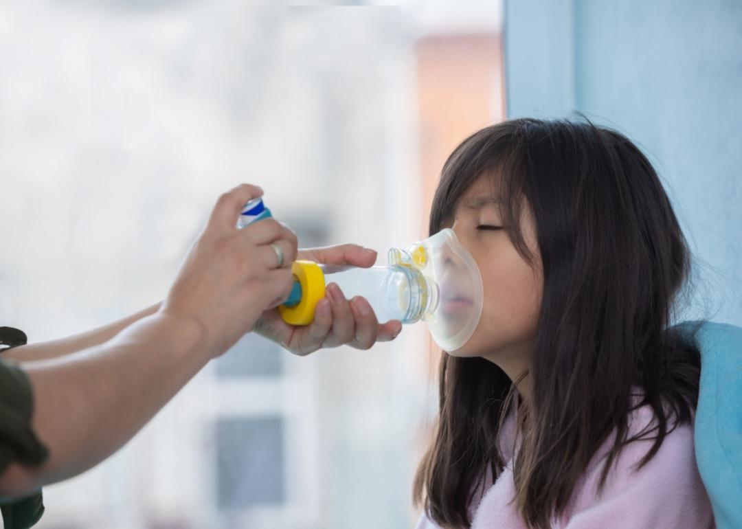 A young girl using a respiratory therapy tool administered by a therapist.