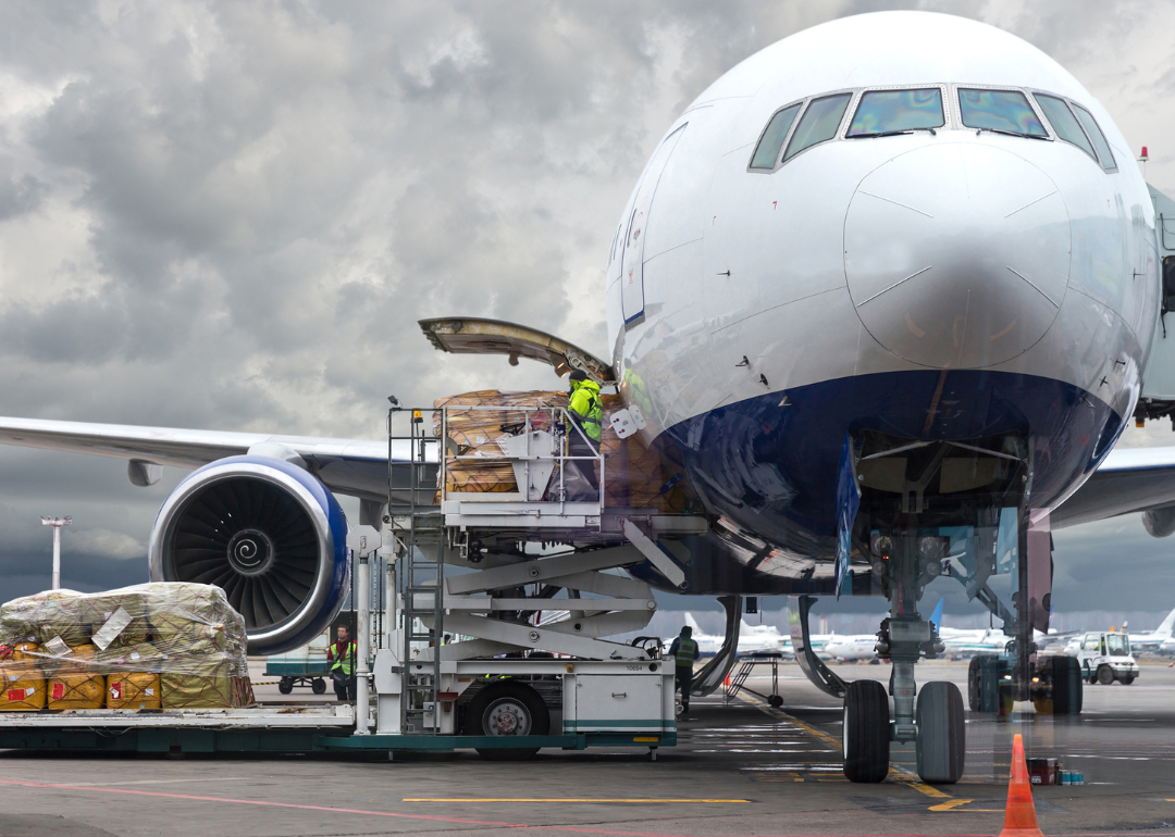 Aircraft cargo handlers moving large packages onto a plane.