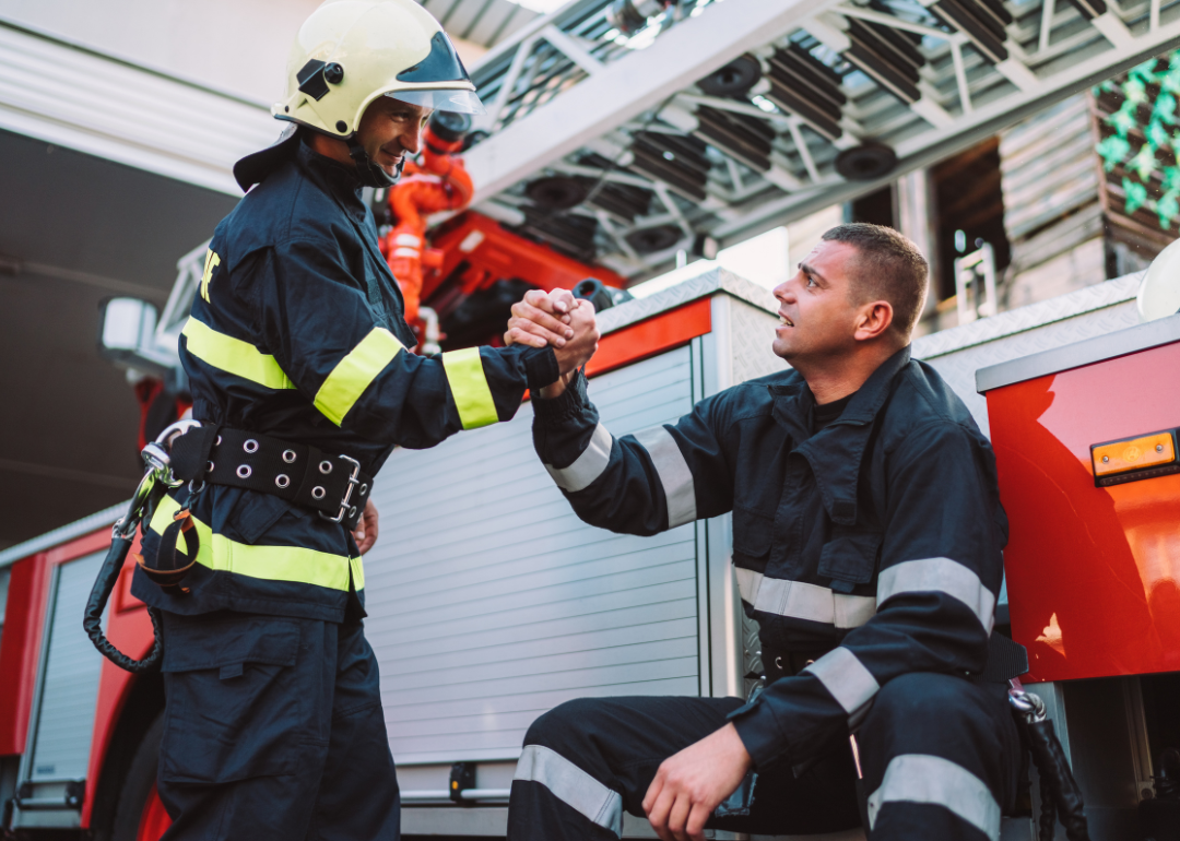 Two firefighters shaking hands in front of an engine.