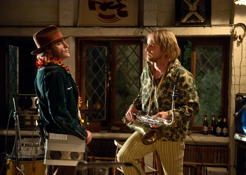Joaquin Phoenix, wearing a recording device on a strap, standing next to Owen Wilson holding a saxophone in Inherent Vice.