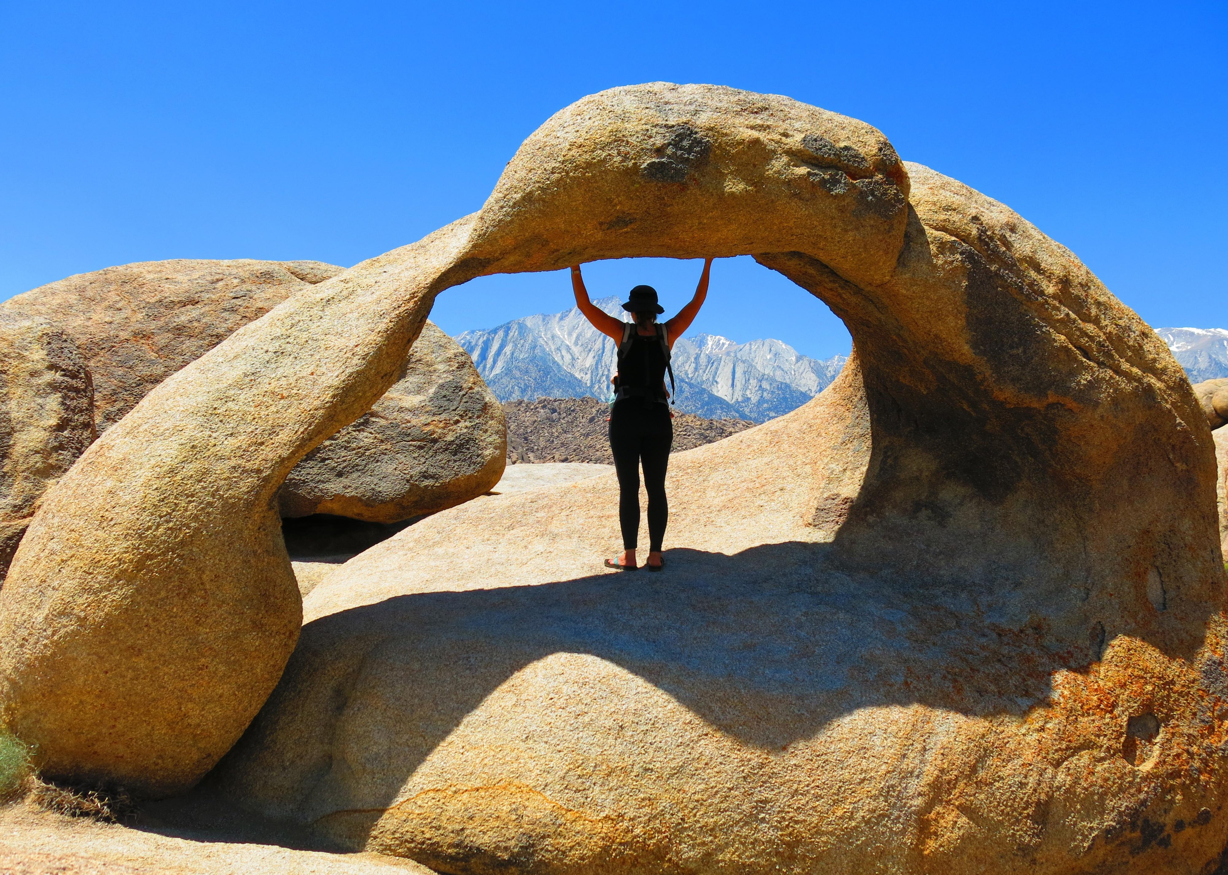 A woman enjoys the view while standing under the archway of a natural rock formation.