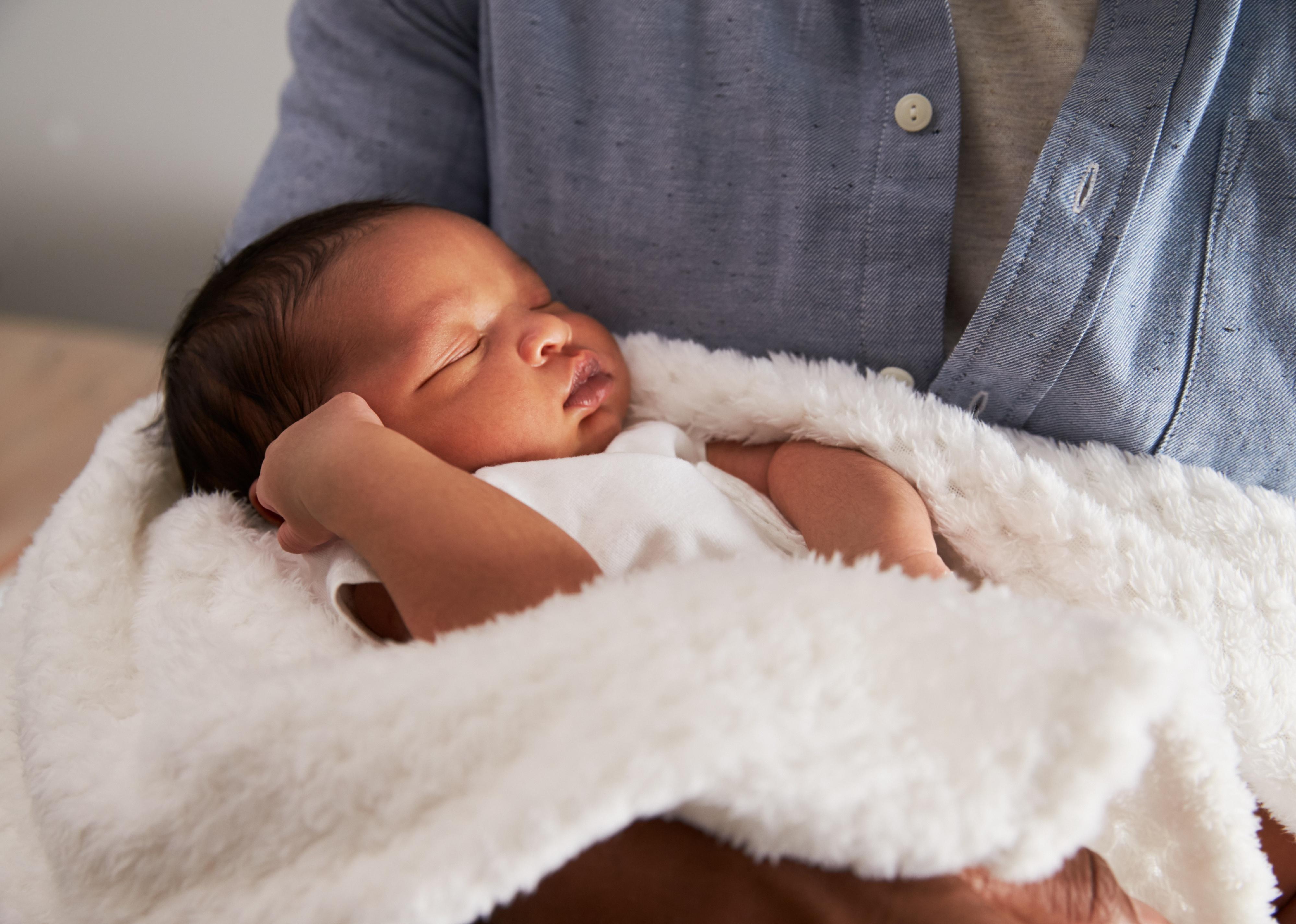 Man holding sleeping baby in white blanket.