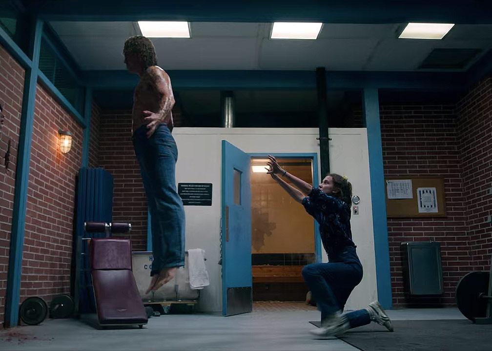 Finn Wolfhard standing shocked against a wall as Dacre Montgomery is lifted up into the air by Millie Bobby Brown's powers.
