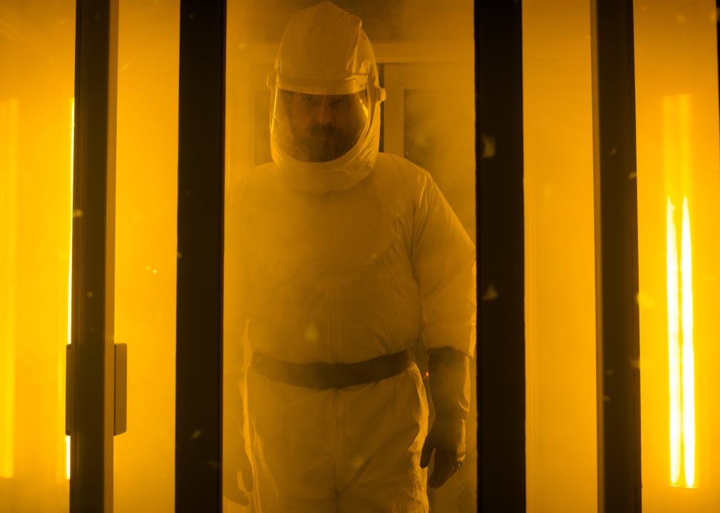 David Harbour wearing a white protective suit in an orange light.